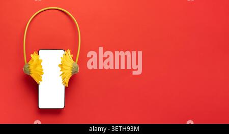 Creative composition of smartphone mockup with yellow flower headphones on bright red background with copy space. Concept of music app, podcast and au Stock Photo