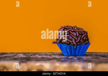 Close-up of a traditional Brazilian chocolate truffle called brigadeiro with sprinkles, served in a blue paper cup over a rustic stone table against a Stock Photo