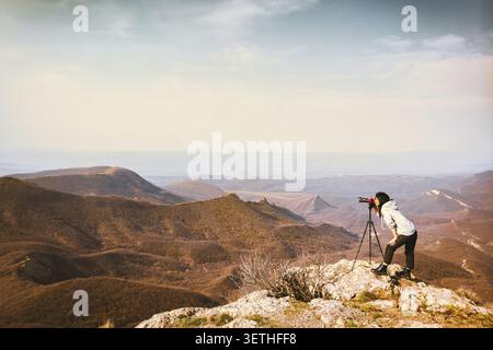 Young passionate attractive caucasian hipster woman content creator photographing mountains with red girly DSLR camera on tripod. Georgia Stock Photo