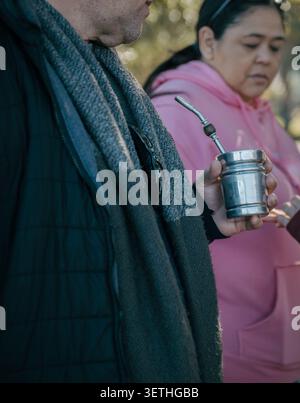 Person holds a metal cup with a straw. Another wears a pink hoodie. Trees blur in the background. The scene is outdoors and calm. Quiet social moments Stock Photo