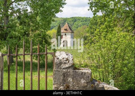 View through an old rusted iron gate of a historic square pigeon tower Pigeonnier with tiled roof and cypress in an idyllic, green summer landscape, P Stock Photo