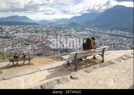 A young couple in love is sitting on a park bench and enjoying the romantic panoramic view of the city and the wide valley from the viewpoint of the B Stock Photo