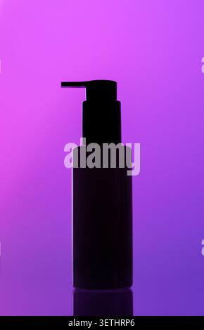 Dark silhouette of bottle with pump dispenser against bright purple-violet gradient background, subtle reflection surface Stock Photo