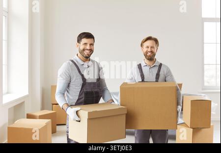 Movers team, service group holding and carrying cardboard boxes, smiling near packed boxes Stock Photo