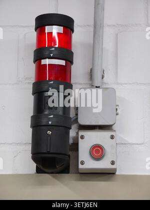 Close-up of industrial red warning beacon assembly mounted on white painted brick wall with metal conduit and junction box Stock Photo