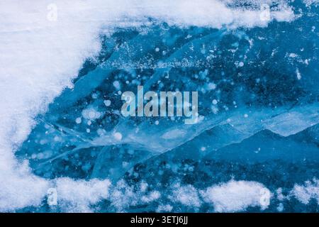 View of Lake Baikal featuring intricate patterns of frozen methane bubbles trapped within the deep blue ice, surrounded by patches of white snow in Se Stock Photo
