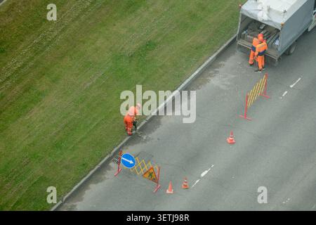 Road crew replacing concrete curb on city street. Workers in uniform orange vest using jackhammer for municipal construction project. Infrastructure i Stock Photo