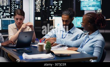 Multiethnic office coworkers reading emails on laptop in boardroom, ensuring project agenda. Cheerful employees analyzing data and KPIs on notebook, statistical information. Office life. Stock Photo
