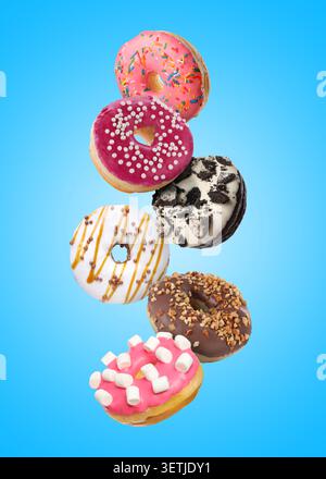 Sweet donuts covered with icing falling on blue background Stock Photo