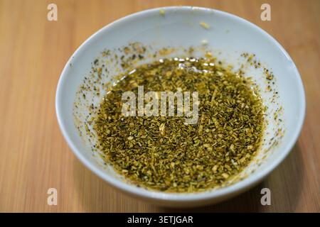 Seasoned olive oil with Mediterranean herbs, garlic, and spices for brushing on oven-roasted vegetables, meat, or potatoes, white bowl on a wooden tab Stock Photo