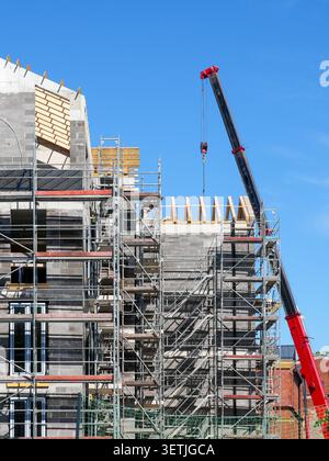 Residential building under construction with scaffolding, crane and timber roof framing on a clear sunny day Stock Photo