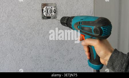 The process of carrying out repairs or electrical installation work indoors. A man's hand holds a turquoise and black cordless screwdriver Stock Photo