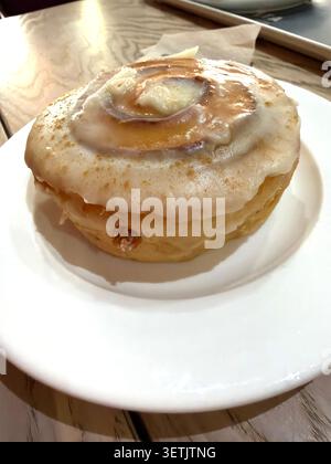 Cinnamon roll with white icing & glaze served on a plate inside a cafe Stock Photo