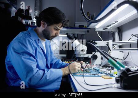 A technician working on circuit board under microscope in lab Stock Photo
