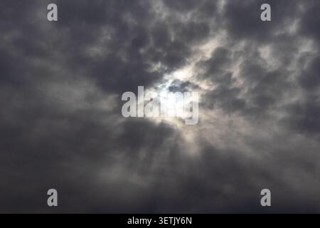 Sun breaking through dark overcast clouds with rays of light spreading across the sky Stock Photo