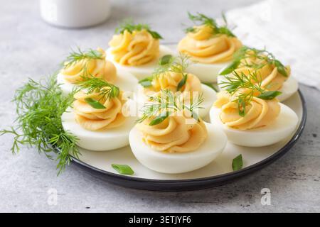 Boiled eggs stuffed with garlic and mayonnaise filling, garnished with fresh dill and green onion. Protein rich appetizer served on a plate, close up Stock Photo