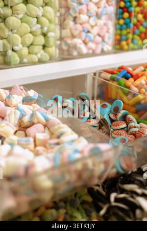 Customers look at different types of candy stored in clear containers in a sweet shop. The scene shows a variety of colors and shapes of candy on disp Stock Photo