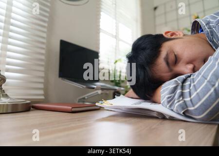 Exhausted Asian man sleeping on desk at office for workplace stress concept Stock Photo