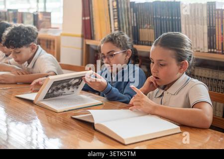 Elementary School Students Reading Books Together in Library Stock Photo