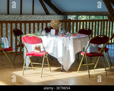 Elegantly decorated reception table prepared for guests in a rustic wedding venue with exposed wooden beams in France. Stock Photo