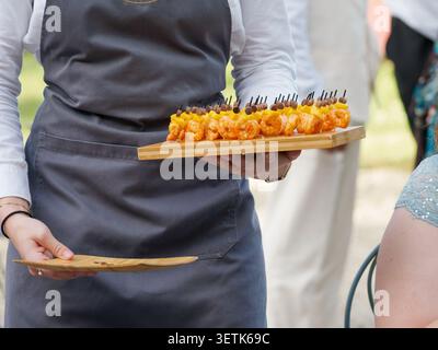 Freshly grilled shrimp served as gourmet appetizers during a catered cocktail reception in France, with chefs preparing and serving the seafood live. Stock Photo