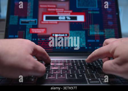 Hacker types on a laptop keyboard and starts an illegal download of sensitive data, computer crime. Hacker types on a laptop keyboard and starts an il Stock Photo