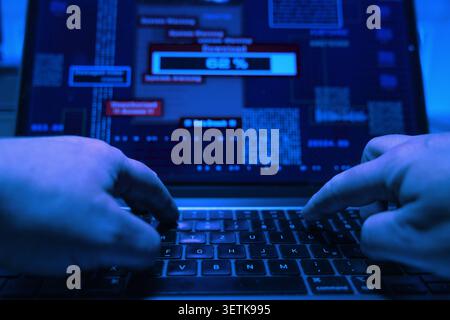 Hacker types on a laptop keyboard and starts an illegal download of sensitive data, computer crime. Hacker types on a laptop keyboard and starts an il Stock Photo