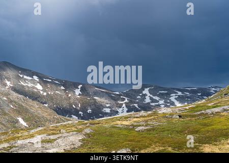 Dramatic storm clouds over snowy mountain peaks and sunny alpine plateau Stock Photo