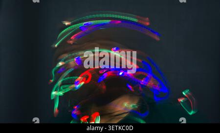 A heavily obscured male figure is engulfed by thick light painting streaks swirling wildly across his head in bright neon red, blue, and green. The in Stock Photo