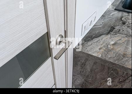 Close-up of a door with a sleek silver handle. Marble countertop and a wall outlet are visible nearby Stock Photo