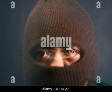 A male subject in a dark brown balaclava faces the viewer with erratic wavy light streaks and horizontal motion blur covering the eye area. The myster Stock Photo