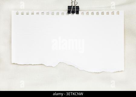 Blank torn notebook paper sheet with binder clip on canvas background. Stock Photo