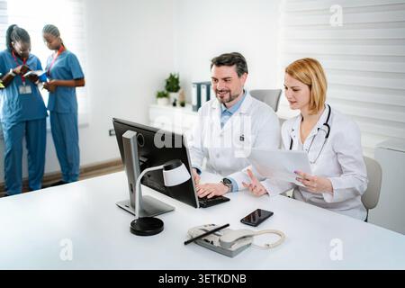 Medical team collaborating and reviewing patient information on computer and documents Stock Photo