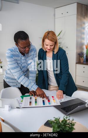 Two diverse designers discussing color swatches at an office desk, illustrating teamwork Stock Photo
