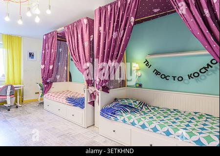 Charming kids' bedroom featuring two canopy beds draped in purple heart-patterned curtains, set against a vibrant blue and yellow backdrop Stock Photo