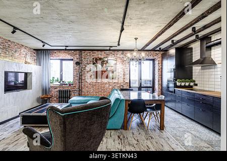 An inviting living space merges industrial chic with modern comfort, featuring exposed brick walls, a blue sofa, and a dark kitchen Stock Photo