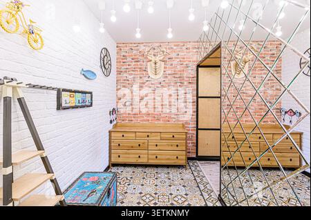 Eclectic room with a mix of textures: brick walls (painted white and natural), wood dressers, and a diamond-patterned mirror wall. Bright bulbs overhe Stock Photo