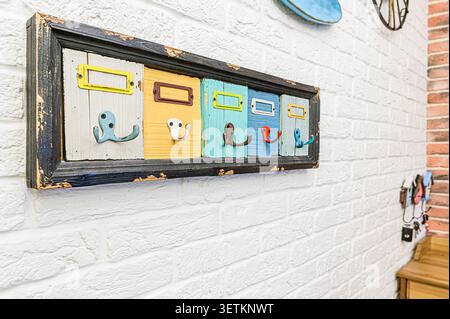 Colorful, rustic coat rack with five hooks, mounted on a white brick wall. Each section is a different color, framed in distressed wood Stock Photo