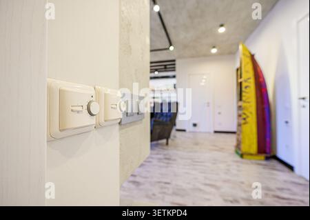 Interior shot with focus on a thermostat and light switches on a wall, leading to a blurred hallway with modern decor Stock Photo