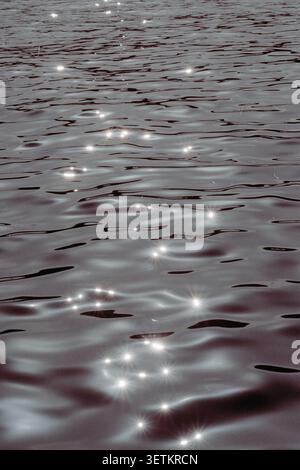 Abstract view of sunlight reflecting on gentle water ripples, creating sparkling highlights and shimmering patterns across the surface. Minimalist nat Stock Photo