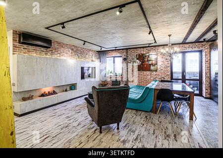Stylish loft-style living room with exposed brick walls, concrete ceiling, modern fireplace, and eclectic furniture Stock Photo