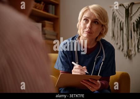 Middle Aged Female Nurse Taking Notes during House Call  Stock Photo
