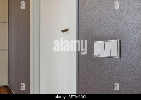 Close-up of a white light switch panel mounted on a textured gray wall, next to a white door with a minimalist handle Stock Photo