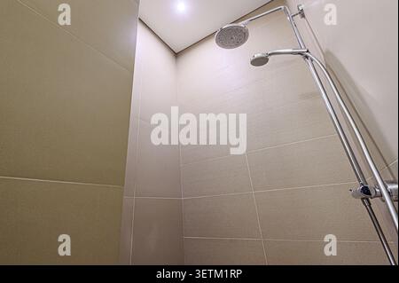 A modern shower featuring beige tile walls and a chrome shower fixture with two showerheads. Clean, contemporary design Stock Photo