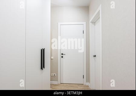 Minimalist interior featuring white walls, two doors, and a wardrobe. The color scheme is predominantly white Stock Photo