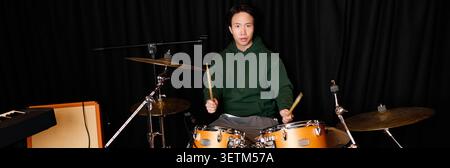 Talented young Asian man plays drums with passion in a vibrant recording studio environment. Stock Photo