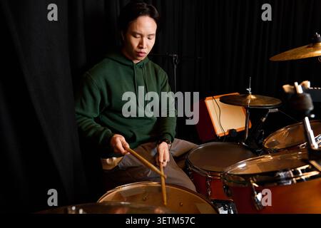Focused young man plays the drums, creating rhythmic magic in a lively studio atmosphere. Stock Photo