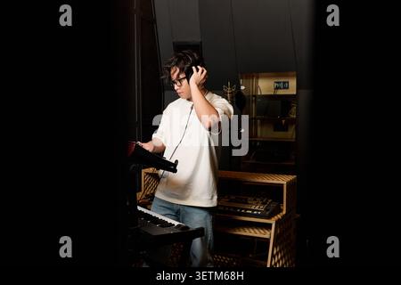 Casual young man immersed in making music, focusing intently in a vibrant recording studio. Stock Photo