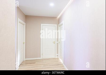 A bright hallway features white doors, light wood flooring, and neutral-toned walls. LED strip lighting adds a modern touch Stock Photo