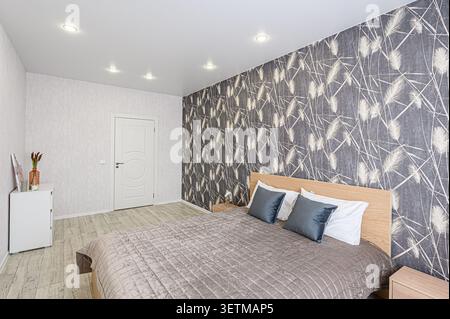 Cozy bedroom with gray patterned accent wall, wooden bed, and soft lighting. Minimalist design with a calming atmosphere Stock Photo